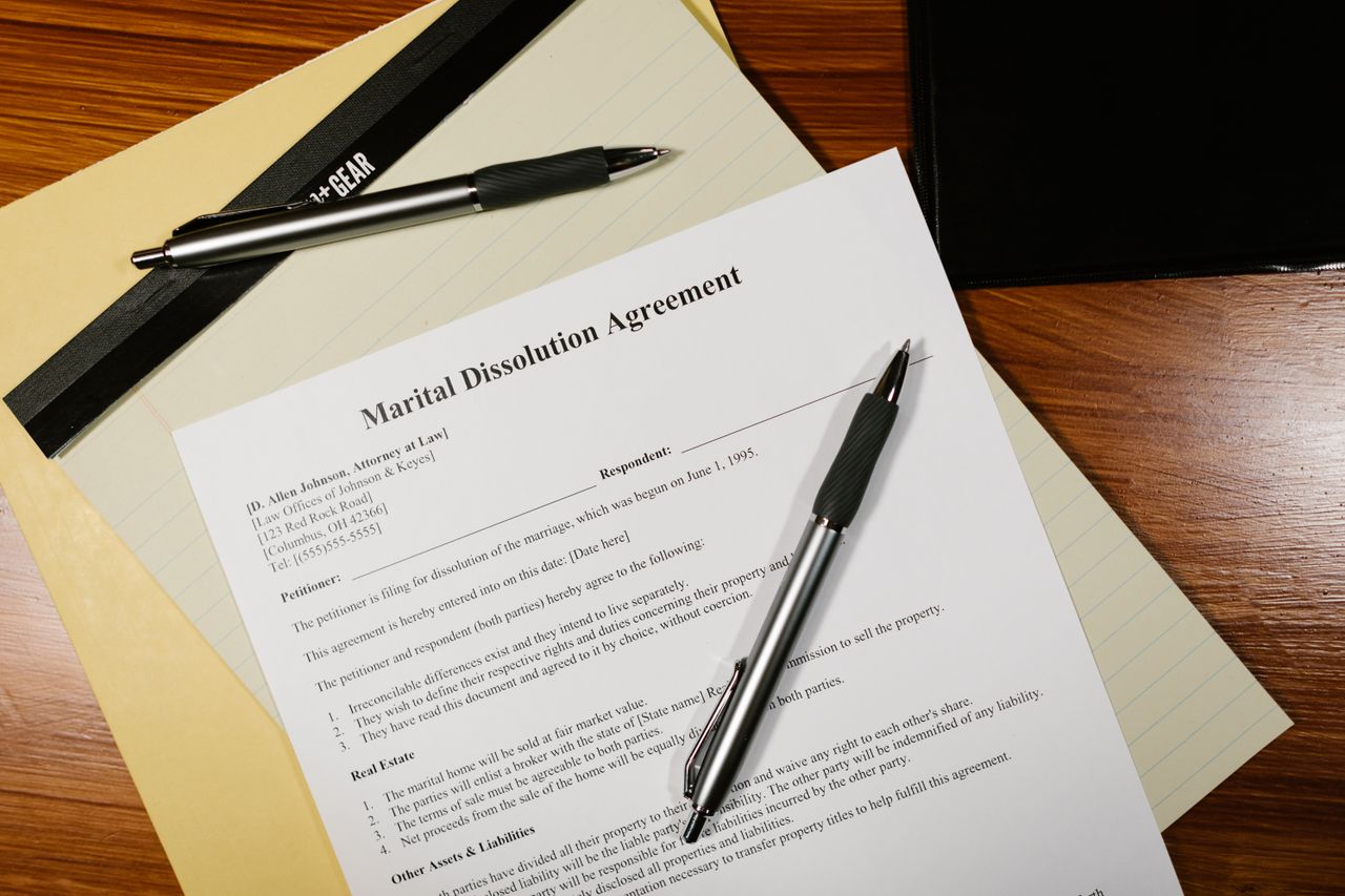 Flat lay of a marital dissolution agreement form with pens and files on a desk.